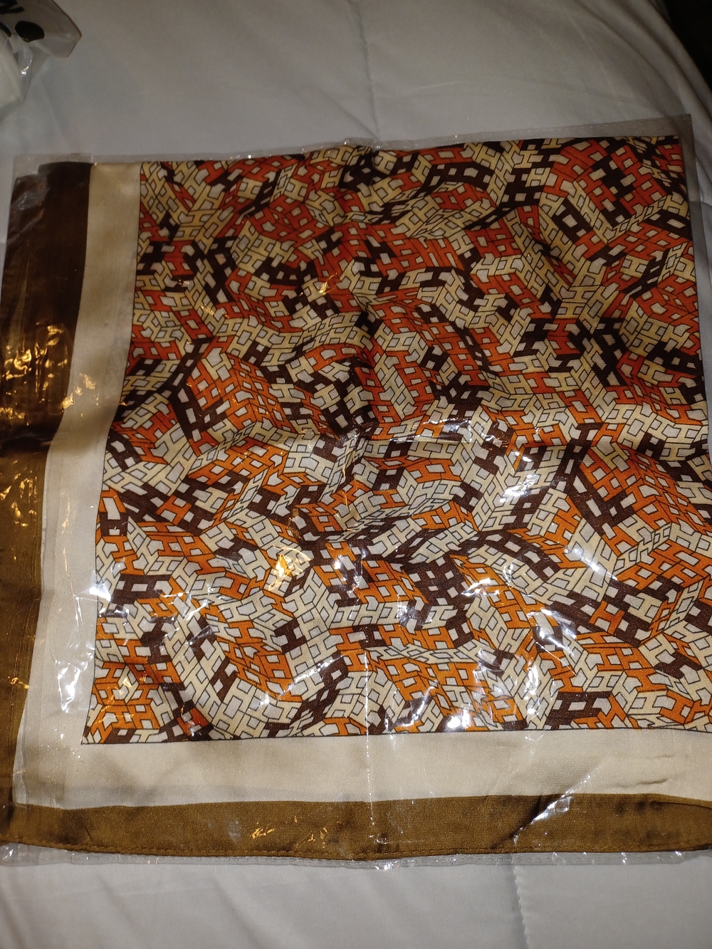 square scarf featuring an intricate geometric letter pattern in shades of orange